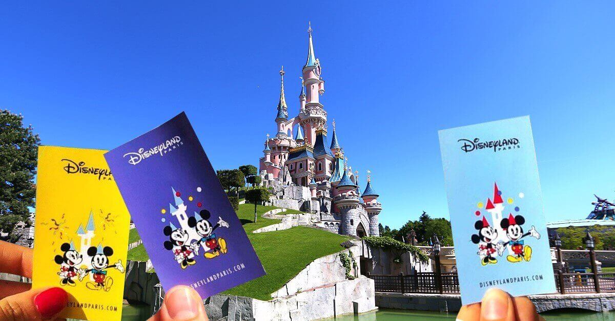 Drei Tickets bzw. Eintrittskarten werden vor dem Schloss von Disneyland Paris in die Luft gehalten